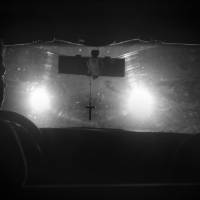 oncoming headlights silhouette crucifix hanging from rear view mirror in this black and white photo